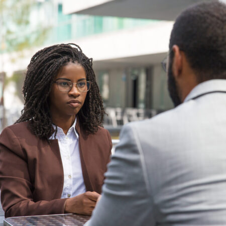 Customer consulting professional in outdoor cafe. African American businesswoman talking to business colleague, sitting at table, listening to him. Consulting concept